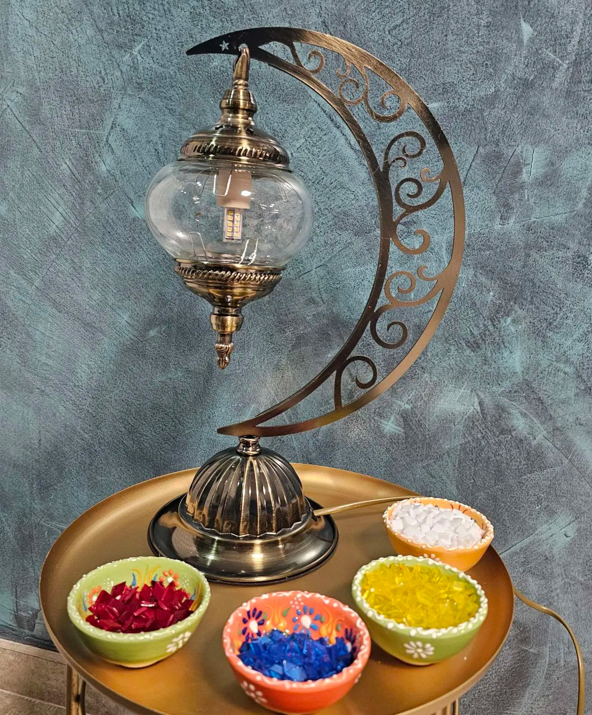 Lampe lune mosaïque artisanale avec globe en verre transparent et perles colorées, création faite main inspirée de l’art turc, posée sur une table avec matériaux de mosaïque autour