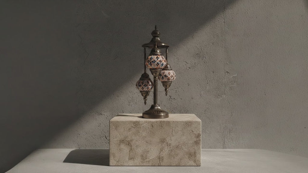 Lampe mosaïque artisanale à trois globes, posée sur un socle en pierre, éclairée par une lumière douce créant une ambiance élégante et haut de gamme.