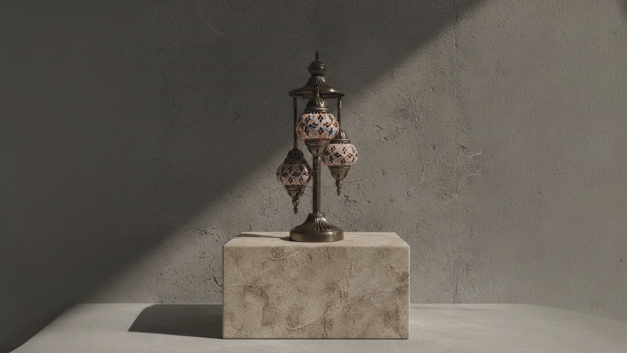 Lampe mosaïque artisanale à trois globes, posée sur un socle en pierre, éclairée par une lumière douce créant une ambiance élégante et haut de gamme.